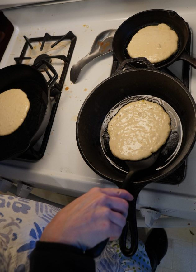 Stove with three cast iron pans cooking vegan pancakes