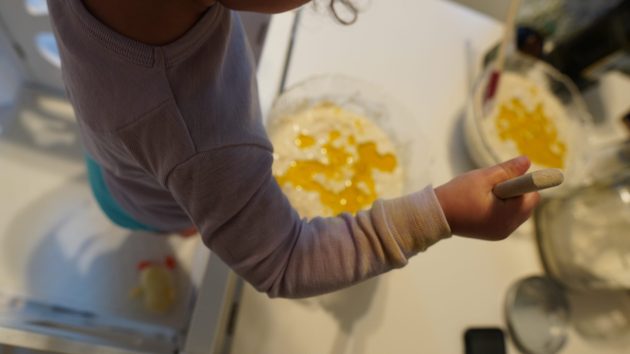 Toddler in learning tower mixing bowl of vegan pancake batter