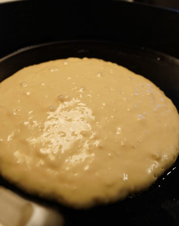 Pancake batter cooking in cast iron skillet