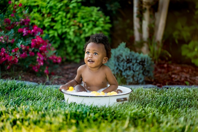 Black baby sittig in a tub on a green yard with plants in the background