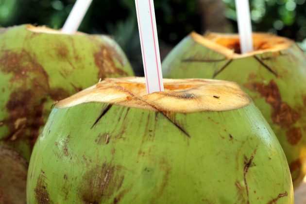 Three green coconuts with straws in them
