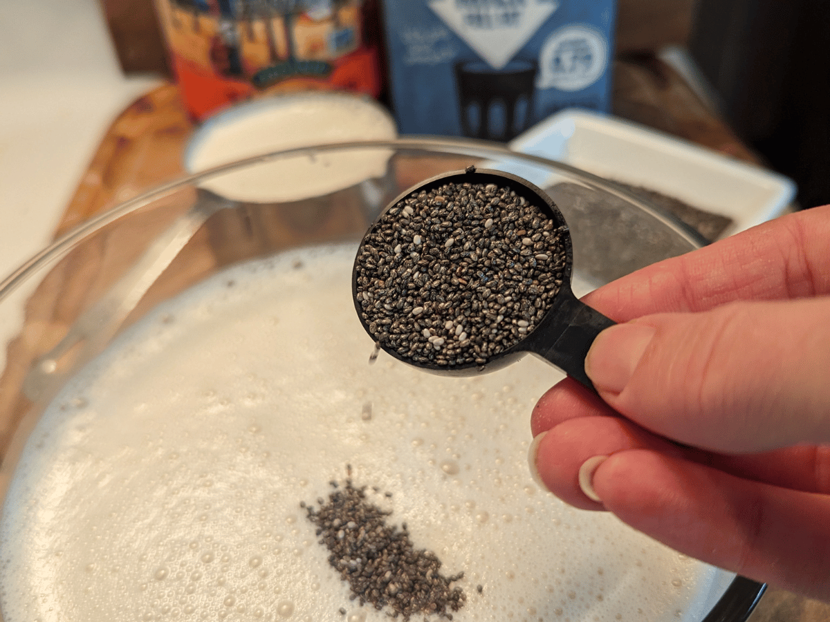 black tablespoon with chia seeds being poured into a glass container with oat milk