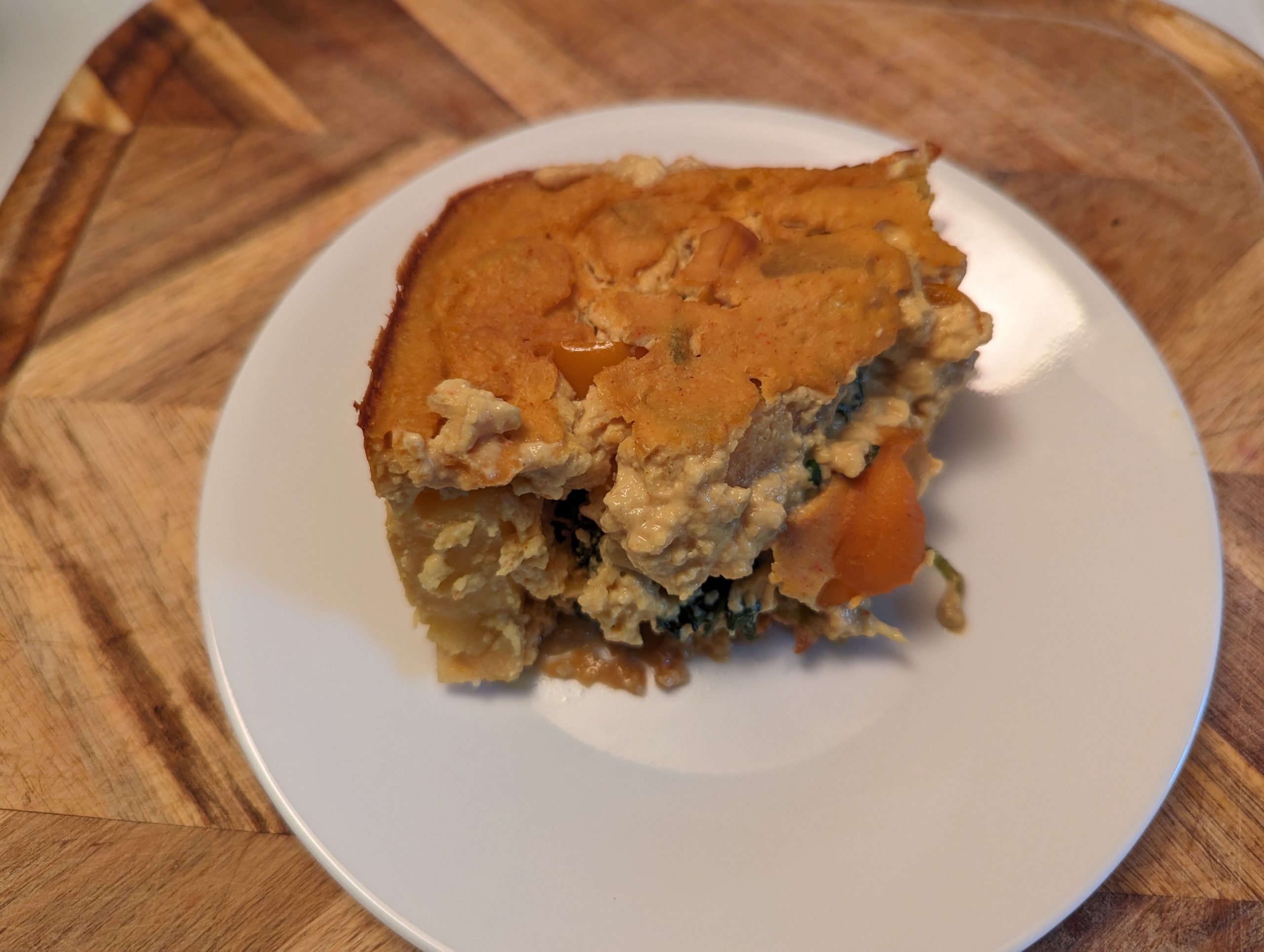 one serving of vegan casserole on a white plate on a wood cutting board