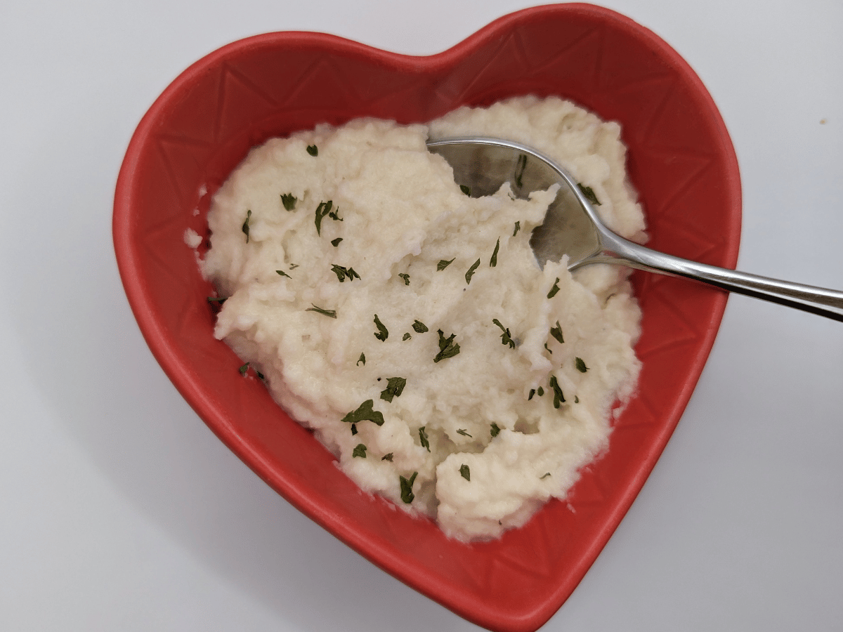 heart shaped red bowl with mashed cauliflower and a spoon